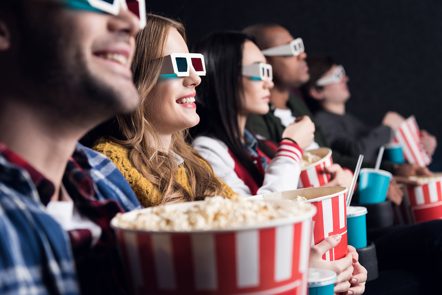 young friends in 3d glasses with popcorn and soda watching movie in cinema