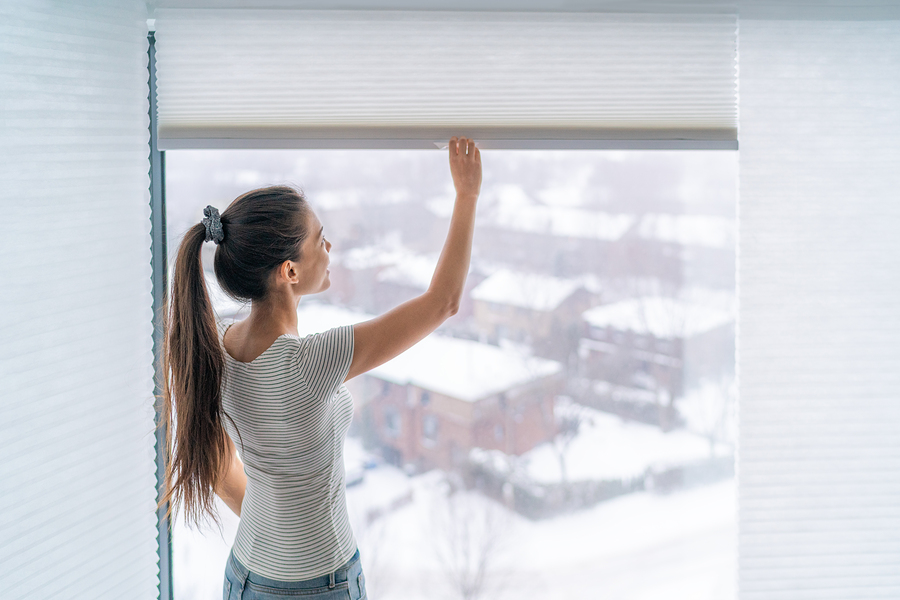 Home blinds window shades woman opening shade blind during winter morning. Asian girl holding modern cordless top down luxury curtains indoors.