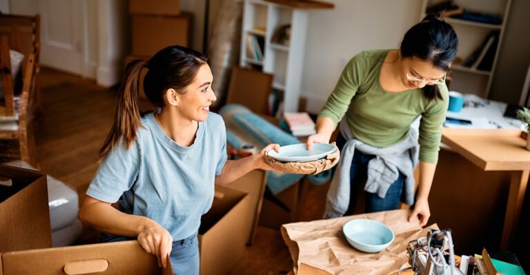 two young women unpacking plates after renting an apartment in Germany